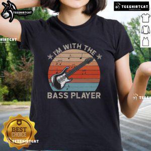 Lady wearing 'Nice I'm With The Bass Player' tee shirt against a sunset backdrop, celebrating music and guitar culture.
