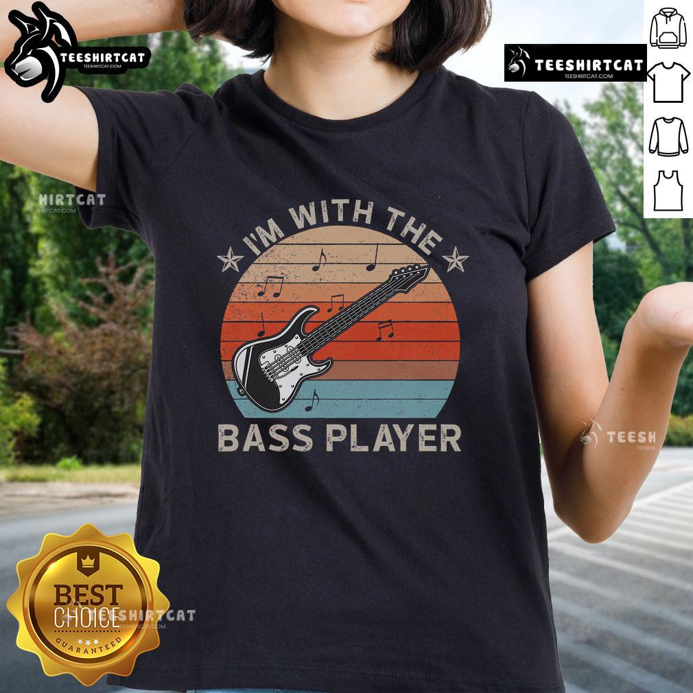 Lady wearing 'Nice I'm With The Bass Player' tee shirt against a sunset backdrop, celebrating music and guitar culture.