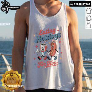Couple enjoying hot dogs together while wearing a 'Nice Eating Hotdogs For Two' tank top at a sunny outdoor picnic.