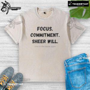 Official Focus Commitment Sheer Will Me in the Book Store washed t-shirt displayed on a wooden shelf with books.