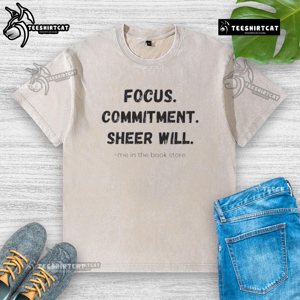 Official Focus Commitment Sheer Will Me in the Book Store washed t-shirt displayed on a wooden shelf with books.